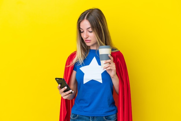 Femme roumaine de super héros d'isolement sur le fond jaune tenant le café à emporter et un mobile