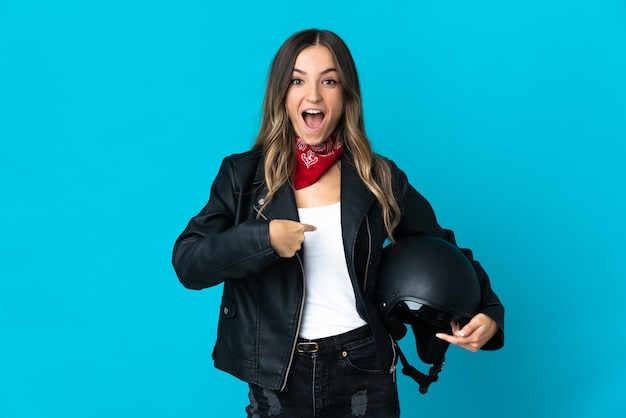 Femme roumaine tenant un casque de moto isolé sur fond bleu avec une expression faciale surprise