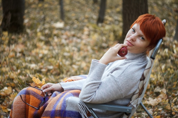 Femme rousse assise dans une chaise longue pliante sur un fond de forêt en automne