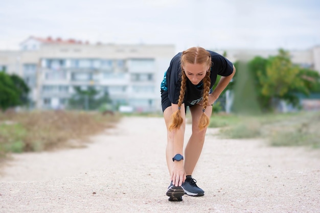 Femme rousse athlétique s'échauffant avant l'entraînement s'étire seul à l'extérieur en été