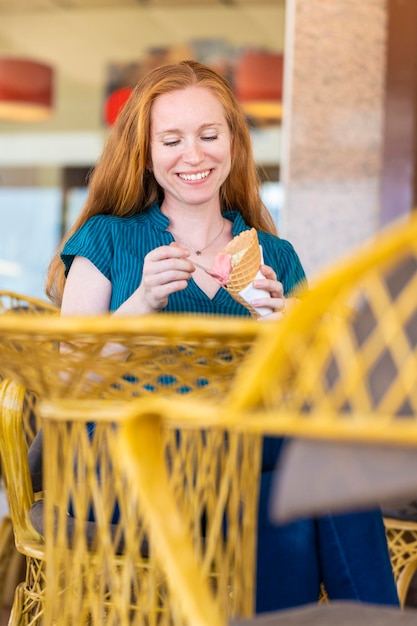 Femme rousse ayant un verre de crème glacée sur une terrasse d'un salon de crème glacée