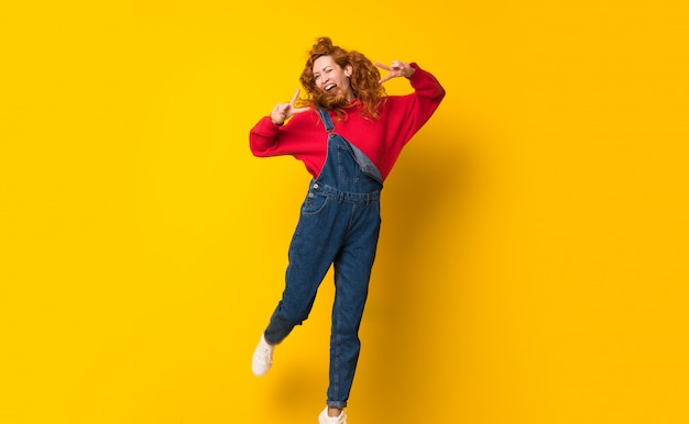 Femme rousse avec une combinaison sautant par-dessus un mur jaune isolé