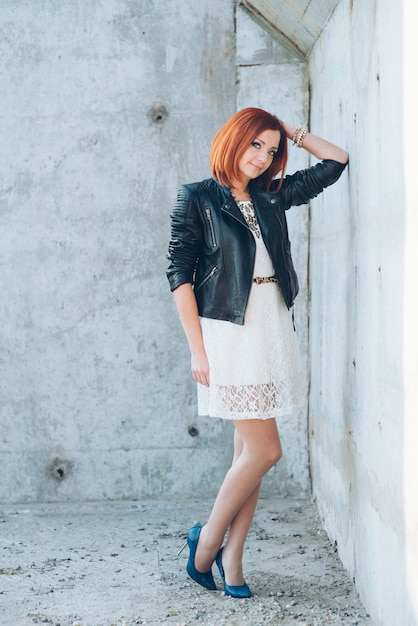 Femme rousse dans une veste en cuir noire sur un mur de béton