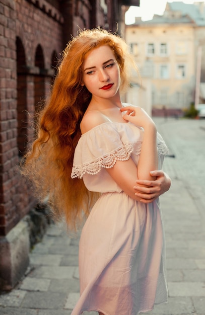 Femme rousse élégante aux cheveux longs vêtue d'une robe blanche aux épaules nues