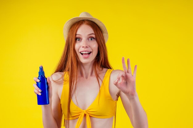 Femme rousse étonnée tenant deux bouteilles en plastique de crème solaire, expression faciale "je ne sais pas". fond jaune studio copyspase.