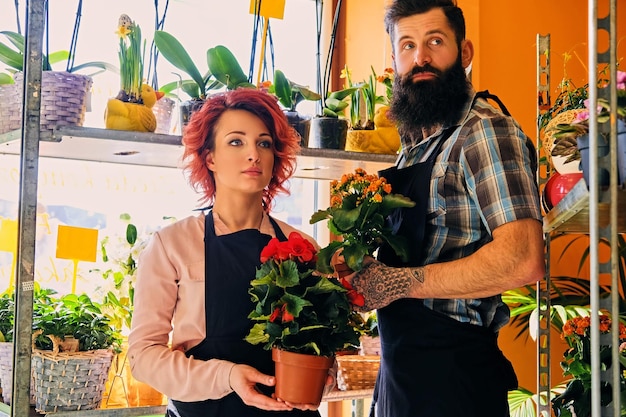 Femme rousse et homme tatoué barbu vendant des fleurs dans un magasin du marché.