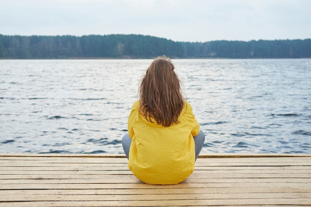 Femme rousse en imperméable jaune assis sur la jetée du lac