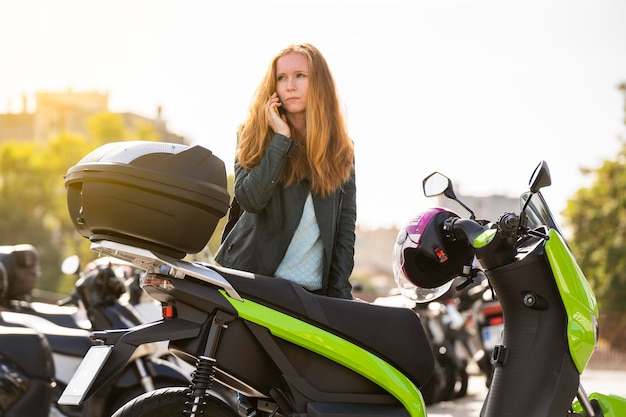 Femme rousse inquiète sur sa moto à l'aide d'un téléphone intelligent