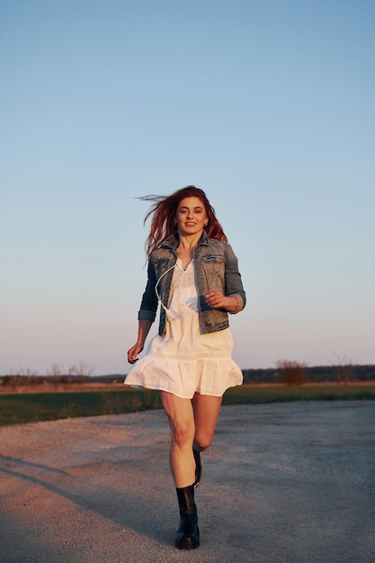 Femme rousse en jupe debout et posant pour un appareil photo sur la route le soir