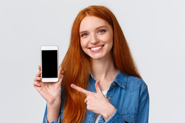 femme rousse montrant l'écran du smartphone et pointant l'écran mobile