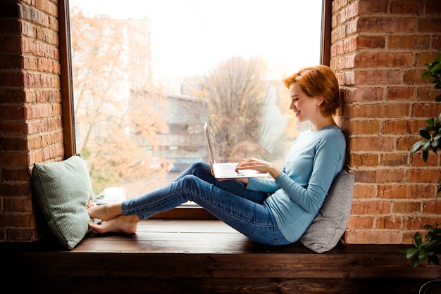 Femme rousse posant près de la fenêtre à la maison