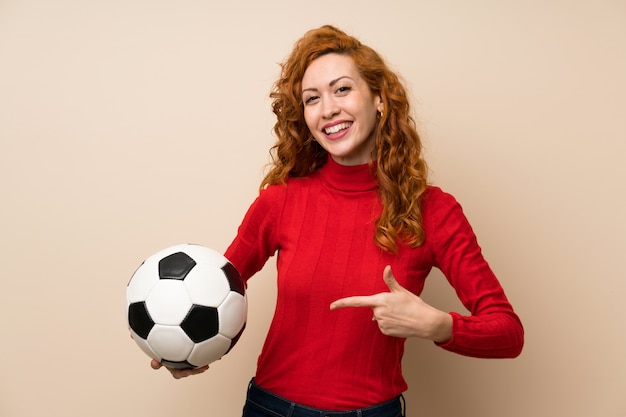 Femme rousse avec un pull à col roulé tenant un ballon de foot