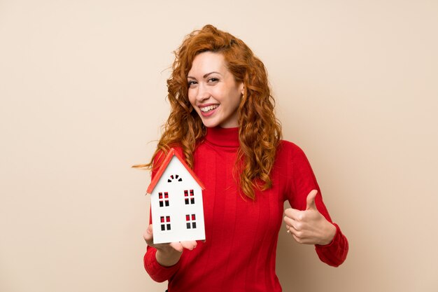 Femme rousse avec un pull à col roulé tenant une petite maison