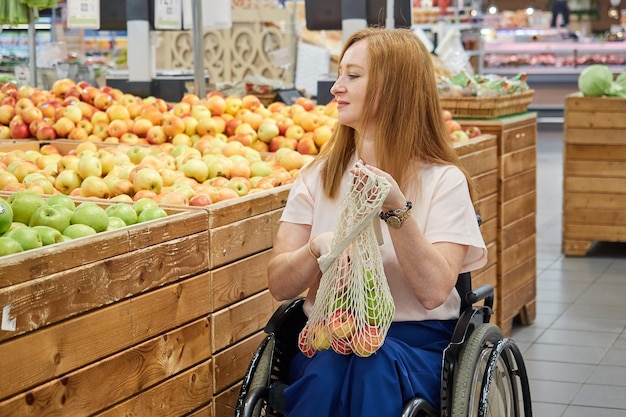 Une femme rousse qui utilise un fauteuil roulant dans un supermarché choisit des fruits