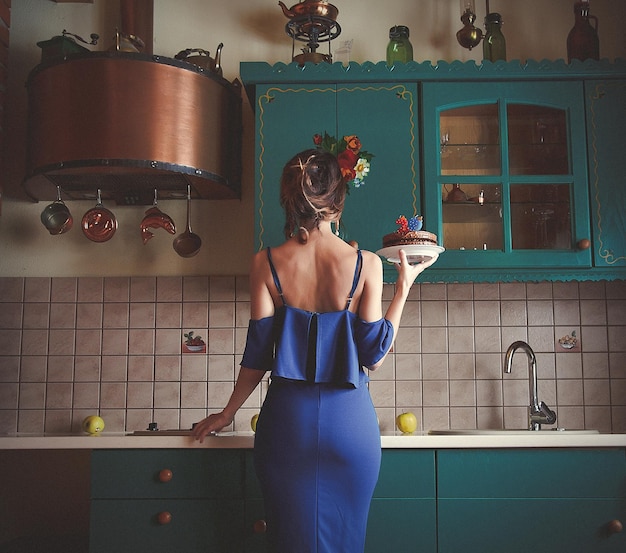 Femme rousse en robe bleue tenant un gâteau au chocolat avec des bougies numéro 29 date d'anniversaire à la cuisine. Image de bruit