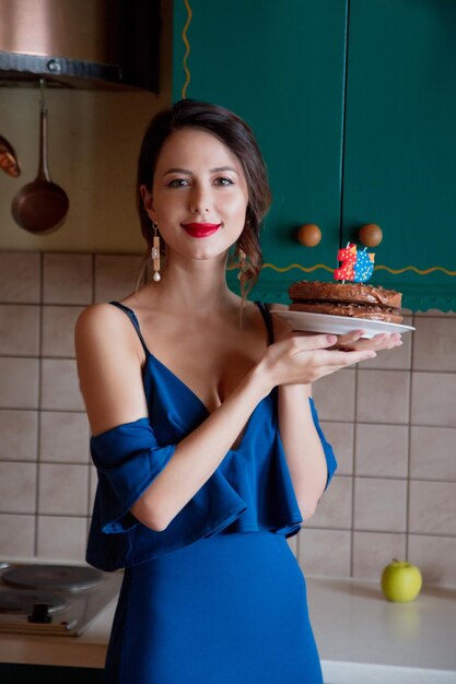 Femme rousse en robe bleue tenant un gâteau au chocolat avec des bougies numéro 29 date d'anniversaire à la cuisine