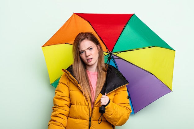 Femme rousse se sentant perplexe et confuse. concept de parapluie