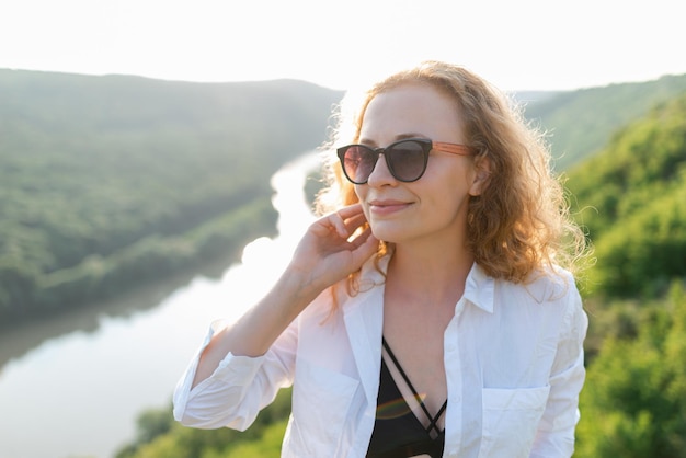 Une femme rousse souriante à lunettes de soleil sur le fond de la rivière Concept de vacances