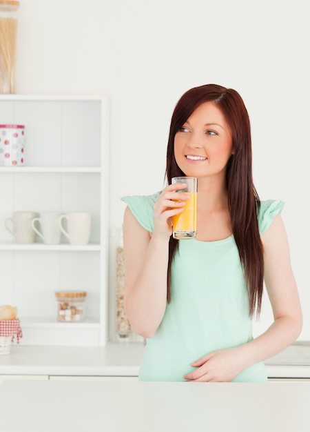 Femme Rousse Souriante Profitant D'un Verre De Jus D'orange Dans La Cuisine