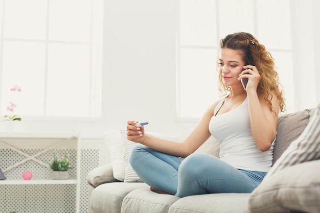 Femme rousse souriante avec test de grossesse. Fille heureuse racontant des nouvelles sur mobile. Concept de famille, d'attente de l'enfant et de maternité. Espace de copie