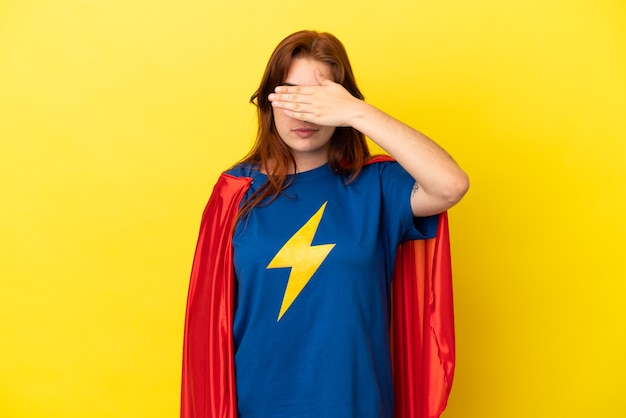 Femme rousse super héros isolée sur fond jaune couvrant les yeux à la main. Je ne veux pas voir quelque chose