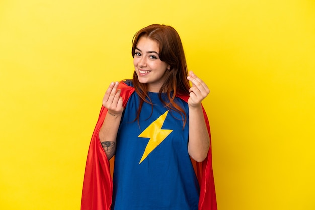 Femme rousse super héros isolée sur fond jaune faisant un geste d'argent