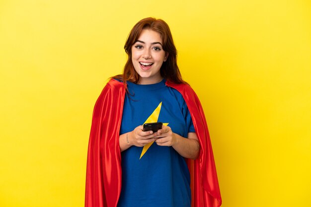 Femme rousse de super héros isolée sur fond jaune surprise et envoyant un message