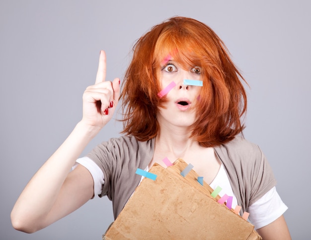 Femme rousse surprise avec livre et notes sur le visage.