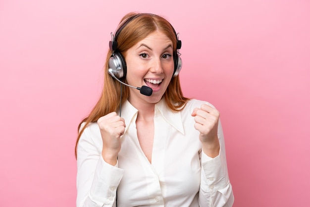 Femme rousse de télévendeur travaillant avec un casque isolé sur fond rose célébrant une victoire en position de gagnant