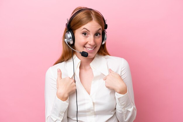 Femme rousse de télévendeur travaillant avec un casque isolé sur fond rose avec une expression faciale surprise