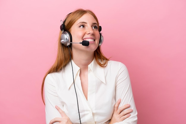 Femme rousse de télévendeur travaillant avec un casque isolé sur fond rose regardant en souriant