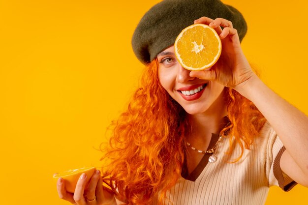 Femme rousse tenant une orange sur fond jaune isolé avec un clin de œil aux fruits