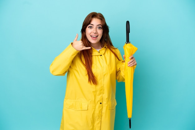Femme rousse tenant un parapluie isolé sur fond bleu faisant un geste de téléphone. Rappelle-moi signe