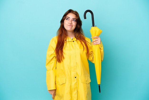 Femme rousse tenant un parapluie isolé sur fond bleu et levant