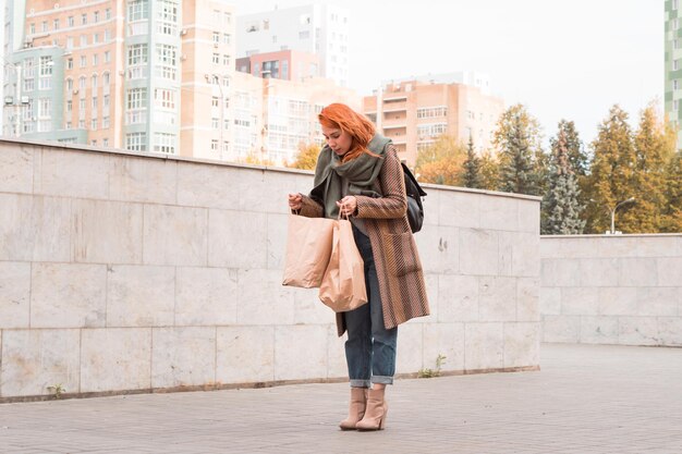 Femme rousse en tenue d'automne avec de gros sacs en papier en ville