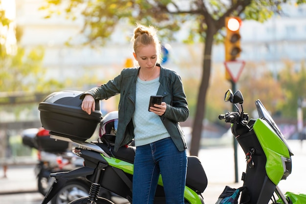 Femme rousse utilisant le téléphone intelligent à côté de sa moto garée