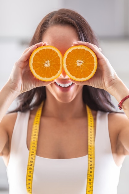 Une femme avec un ruban à mesurer autour du cou tient une orange coupée en deux devant ses yeux