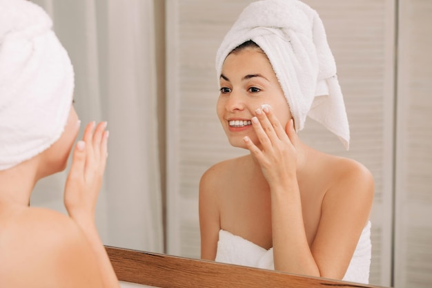 Une femme s'applique de la crème sur le visage dans la salle de bain