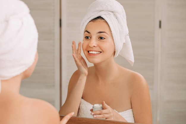 Une femme s'applique de la crème sur le visage dans la salle de bain