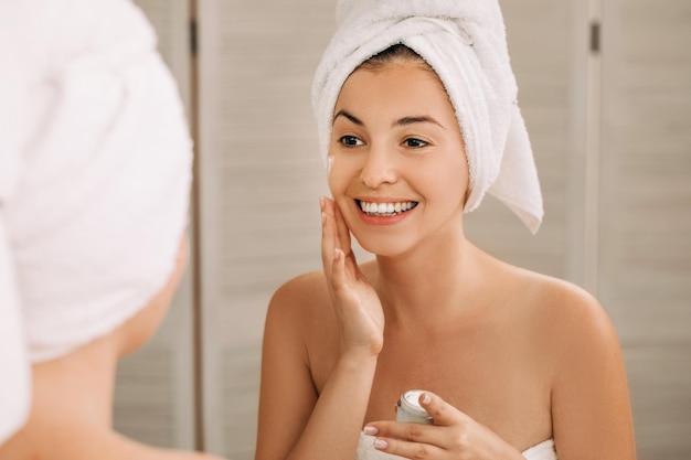 Une femme s'applique de la crème sur le visage dans la salle de bain