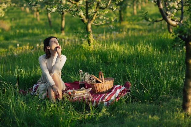 La femme s'assied sur la couverture au pique-nique et mange la pêche