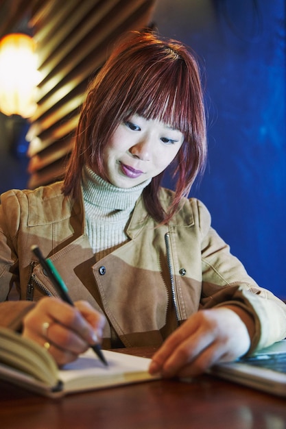 La femme s'assied pensivement écrivant dans un cahier dans un restaurant