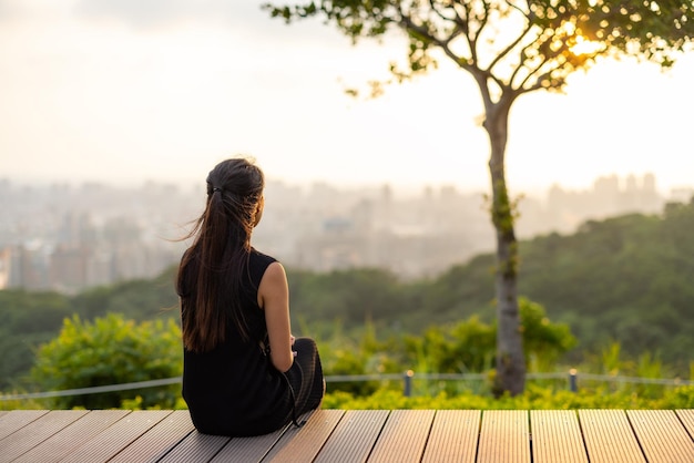 La femme s'assoit sur le banc de bois et regarde le coucher de soleil