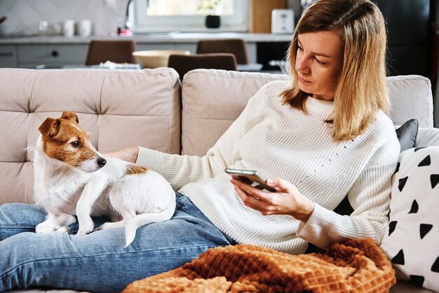 Une femme s'assoit avec un chien et utilise un smartphone