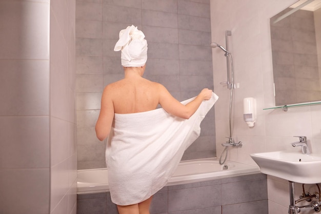 Une femme s'essuie avec une serviette après la douche et enlève une serviette blanche pour prendre un bain ou une douche