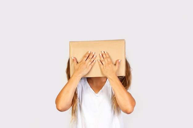 Femme avec sa tête dans une boîte et couvrant les deux yeux geste debout sur un fond blanc