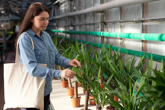 Femme avec un sac en coton écologique choisissant le yucca à la serre