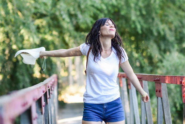 Femme avec sac à dos, debout sur un pont rural.