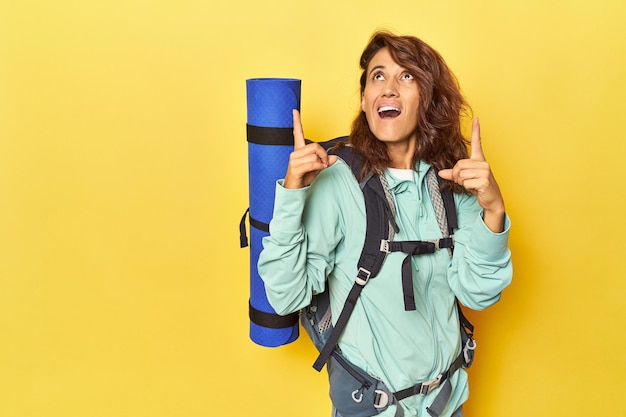 Femme avec sac à dos de randonnée et tapis sur jaune pointant vers le haut avec la bouche ouverte