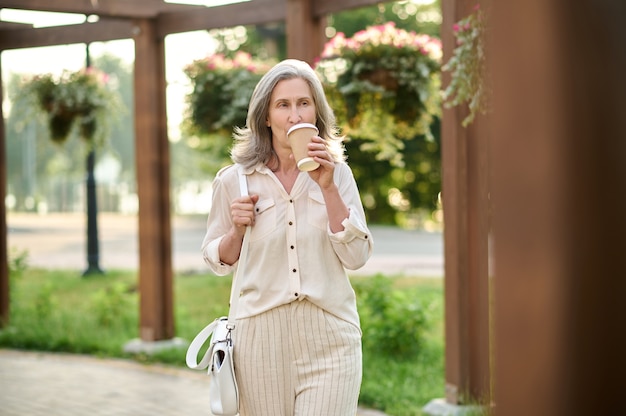 Femme avec sac à main buvant du café dans le parc